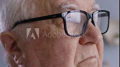Close up portrait of a gray-haired confident thinking elderly man wearing eyeglasses looking to the side standing indoors. Concentrated old male senior person in retirement. 4k video.