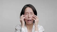 Unhappy Korean Mature Woman Touching Face Making Facial Massage Caring For Aging Skin With Wrinkles Looking At Camera Posing Over Gray Background, Studio Shot. Beauty Care And Cosmetics
