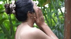 Side view footage of Asian woman smiling and reaching out her palm while taking bath under shower in an outdoor shower room