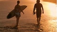 SILUETA AÉREA: Dos surfistas llevando tablas de surf y revisando olas después de la sesión de surf. Amigos surfistas caminando en la playa en la luz dorada. Hermoso paisaje de verano en Playa Venao en Panamá.