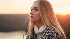 Portrait of attractive blond woman with long hair in blanket looking at the camera with incredible pink sunset on the background.
