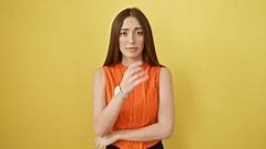 Nervous hispanic woman in sleeveless t-shirt, stressed and biting nails, isolated on a yellow background, indicative of anxiety problem