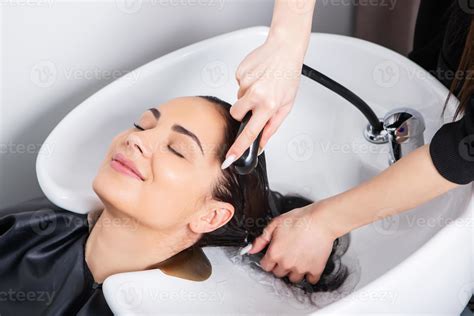 professional hairdresser washing hair of young woman in beauty salon ...