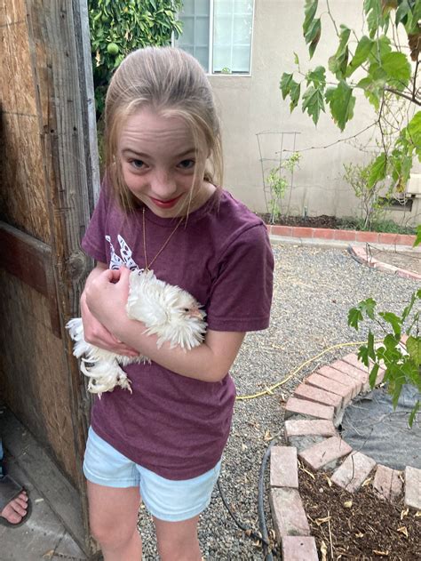 Blonde Girl with ponytail holding pet chicken in fro...