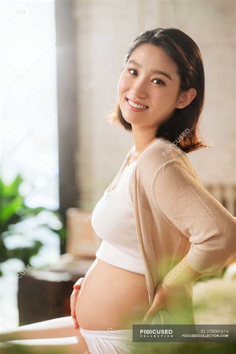 Side view of happy young pregnant asian woman smiling at camera ...