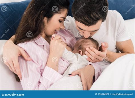 Young Mother Breastfeeding Little Baby with Husband Near by on Bed ...