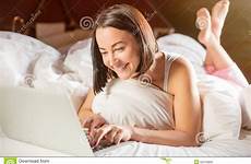 bed lying woman laptop her legs down raised slightly smiling front