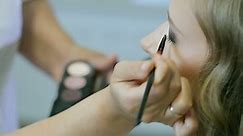 Professional makeup artist applying tonal powder to long curl hair blond models with blue eyelid. Closeup view.