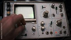 A vintage oscilloscope displays a vibrant green waveform on its screen. The footage highlights the retro aesthetic of analog technology and the visual representation of electronic signals.