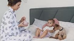 young mother spoon-feeds her baby girl sitting on the bed with a Yorkshire Terrier dog beside