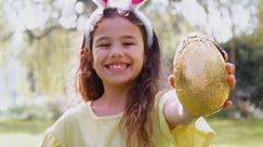 Premium stock video - Portrait of girl wearing bunny ears holding chocolate egg on easter egg hunt in garden