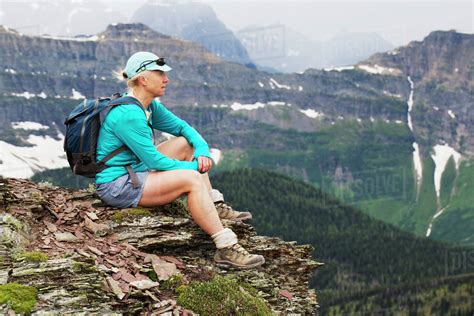 Female hiker sitting on a rock cliff overlooking the valley with a ...