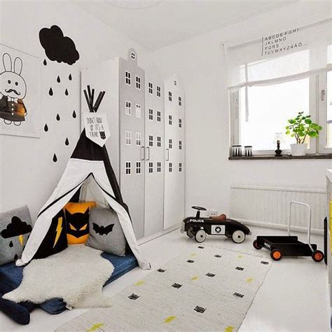 Black and white attic playroom features a ceiling and walls clad in urban walls plus signs decals lined with charcoal gray tufted cushions lined with pillows illuminated by yellow sconces facing a pair of rope and wood swings suspended from the ceiling. black-and-white-kids-room-with-tents