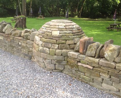 Building a dry stone retaining wall. Boundary wall of a pub featuring a dry stone sculpture, in ...