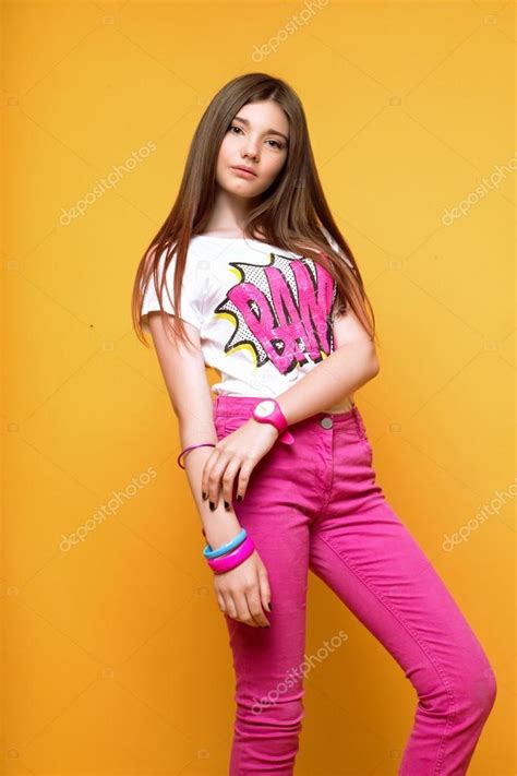 Archivfotos herunterladen 13 years girl. A beautiful 13-years old girl dressed in pink pants and a T-shirt in studio on yellow background ...