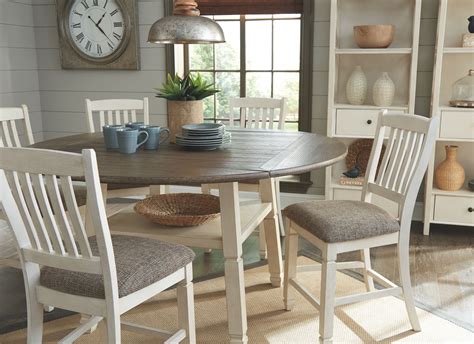 Beach style dining room features a shiplap ceiling accented with rustic wood beams accented with a wood chandelier, arteriors manning chandelier, placed over a round dining table lined with white slipcovered dining chairs. Bolanburg 5-Piece Counter Height Dining Room, Antique ...